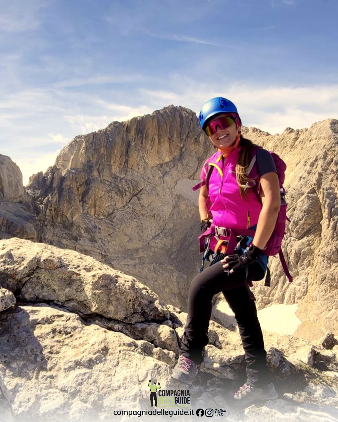 Persona con casco blu e imbracatura su terreno roccioso in montagna.